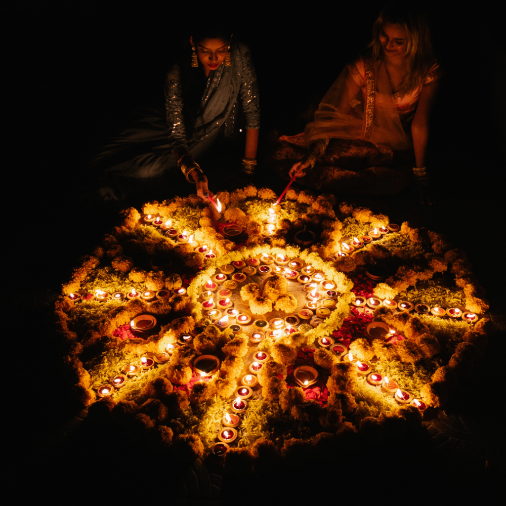 Cercle de femmes assises et souriantes autour d'un autel de fleurs et de bougies dans la nuit. Sororité, féminité, empowerment